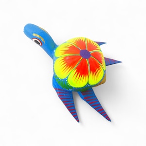 Może przedstawiać: Ręcznie malowana drewniana figurka żółwia. Żółw ma niebieski korpus, nogi i głowę, z czerwono-niebieskimi paskami na nogach. Skorupa jest żółta, czerwona i fioletowa, z kwiatowym wzorem. Figurka jest przedmiotem dekoracyjnym.