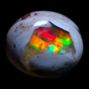 May include: A polished, rounded boulder opal gemstone featuring a smooth, off-white, and tan exterior shell. A central, recessed cavity reveals a vibrant, multi-colored play-of-color with intense flashes of neon red, orange, yellow, and green.
