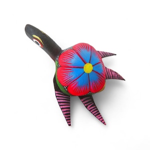 Może przedstawiać: Ręcznie malowana drewniana figurka żółwia. Ciało i głowa są czarne, a skorupa ma kwiatowy wzór w kolorze czerwonym, niebieskim i żółtym. Nogi są różowe z czarnymi paskami. Unikalny kawałek sztuki ludowej.