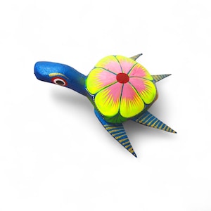 Może przedstawiać: Ręcznie malowana drewniana figurka żółwia. Żółw ma niebieską głowę i nogi, żółto-różowy pancerz z czerwonym środkiem i złote akcenty. Na białym tle.