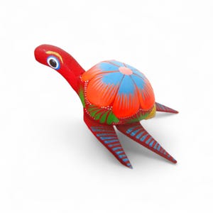 Może przedstawiać: Ręcznie malowana drewniana figurka żółwia. Żółw ma czerwoną głowę i nogi, skorupę z pomarańczowymi i niebieskimi wzorami kwiatowymi oraz niebieskie paski na nogach. Figurka jest ozdobiona szczegółowymi, żywymi kolorami.