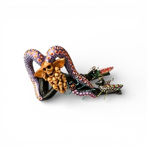 May include: A handcrafted, whimsical sculpture featuring a purple octopus with orange and white spots, a skull, and several smaller skulls. The sculpture is mounted on a dark branch with colorful insect figures.