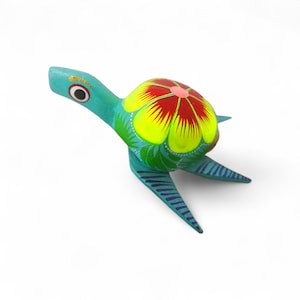 Może przedstawiać: Ręcznie malowana drewniana figurka żółwia. Żółw ma turkusowy korpus, żółto-czerwony kwiatowy wzór na skorupie i niebieskie paski na płetwach. Głowa żółwia jest turkusowa z czarno-białym okiem.