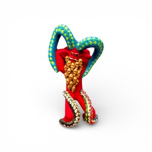 May include: A vibrant, handcrafted sculpture of a red creature with blue and yellow patterned horns and tentacles. The creature has a cluster of gold skulls on its chest and is posed on a white background.