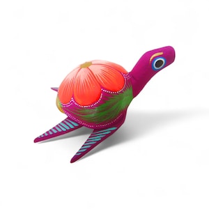 Może przedstawiać: Ręcznie malowana, dekoracyjna figurka żółwia. Korpus jest w kolorze magenta, skorupa zaprojektowana jest tak, aby przypominała kwiat w odcieniach pomarańczu i czerwieni, z zielonymi akcentami. Płetwy mają niebieskie paski.