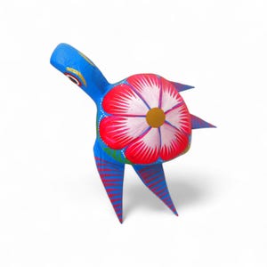 Może przedstawiać: Żywa, ręcznie malowana drewniana rzeźba ludowa przedstawiająca zwierzę z dużym kwiatowym wzorem na grzbiecie. Rzeźba ma niebieski korpus z czerwono-białymi paskami na nogach i czerwono-biały kwiatowy wzór.