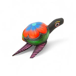 Może przedstawiać: Ręcznie malowana drewniana figurka żółwia. Skorupa żółwia jest ozdobiona niebieskim kwiatowym wzorem z pomarańczowymi i czerwonymi płatkami. Głowa i nogi żółwia są czarne, a nogi mają różowe i czarne paski.