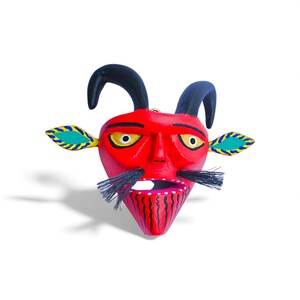 May include: A vibrant red devil mask with black horns and mustache. The mask features yellow eyes, leaf-shaped ears with blue and yellow accents, and a detailed mouth. This handcrafted mask is likely for a costume or decorative purpose.