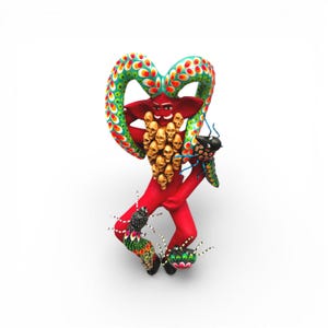May include: A vibrant, handcrafted folk art sculpture of a red figure with a heart-shaped head and a cluster of golden skulls. The figure has green and red patterned accents and is adorned with colorful insect-like creatures.