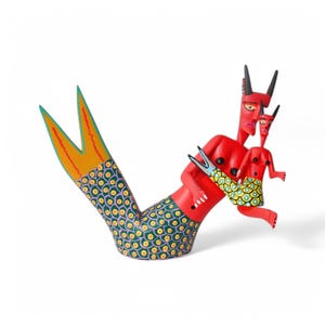 May include: A red wooden mermaid with a green and yellow patterned tail, holding a smaller red mermaid with a green and yellow patterned tail.