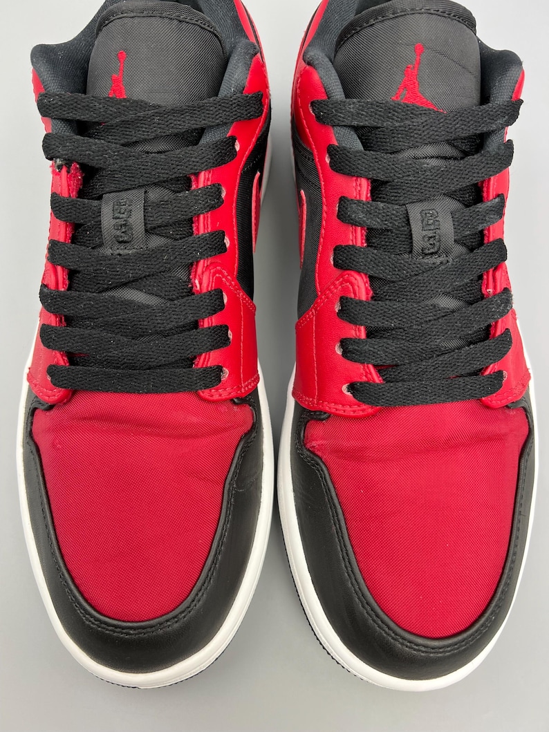 Puede incluir: Par de zapatillas rojas, negras y blancas. Las zapatillas tienen tela roja en la puntera y los paneles laterales, revestimientos de cuero negro y cordones negros. La leng&uuml;eta y el cuello son negros, con un logotipo rojo en la leng&uuml;eta.