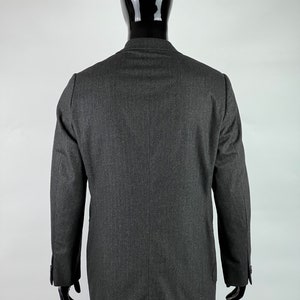 May include: A dark gray blazer with a single button closure and long sleeves. The blazer is made of a textured fabric and has a classic fit.