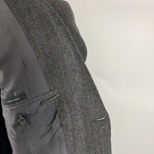 May include: A gray pinstripe blazer with a black lining and a single button on the left side. The lining has the text "Tailor Made" printed on it.