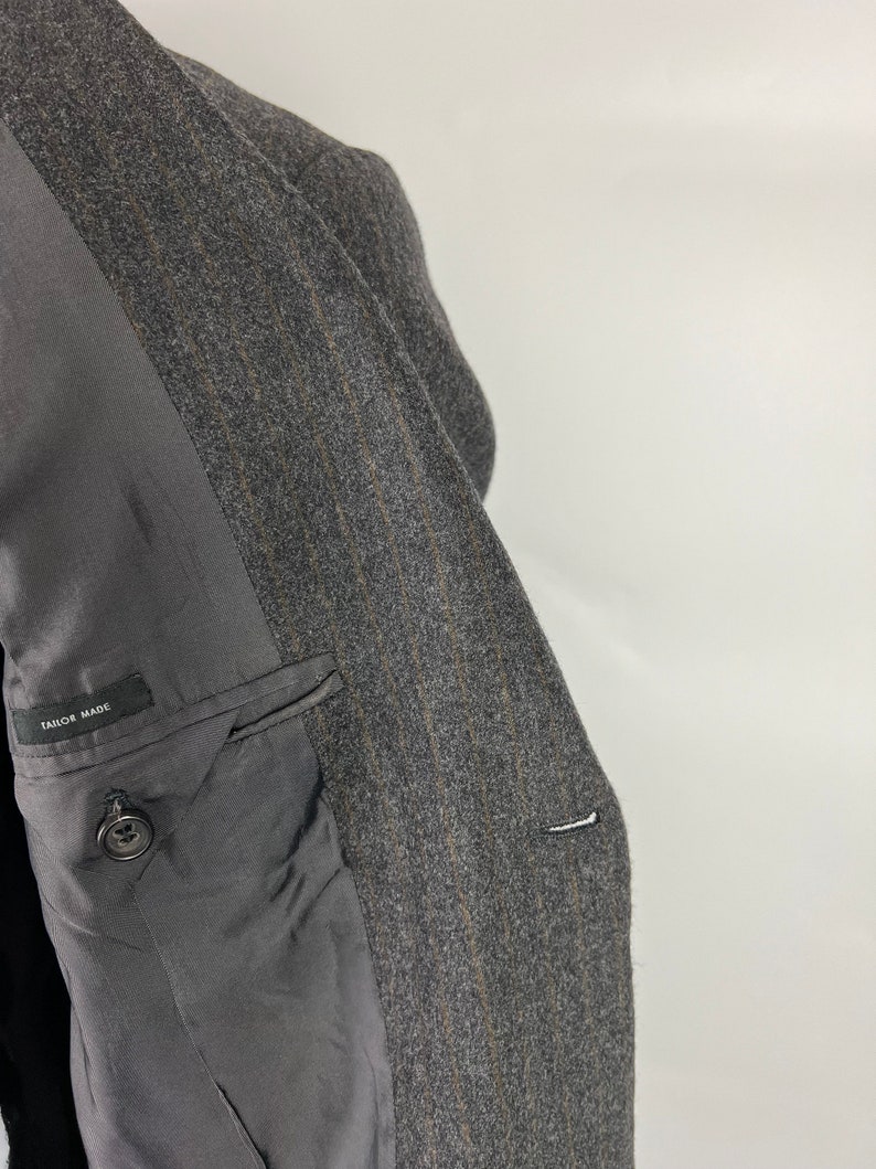 May include: A gray pinstripe blazer with a black lining and a single button on the left side. The lining has the text "Tailor Made" printed on it.