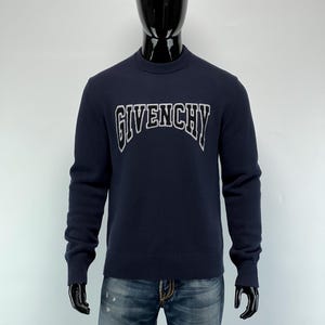 Pode incluir: Camisola azul marinho com a palavra "GIVENCHY" em letras brancas arqueadas no peito. A camisola tem gola redonda e mangas compridas. A modelo usa calças de ganga azuis.