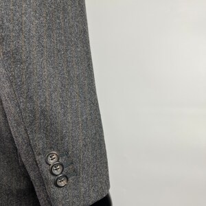 May include: A gray blazer with thin brown stripes. The blazer has a three-button cuff on the sleeve.
