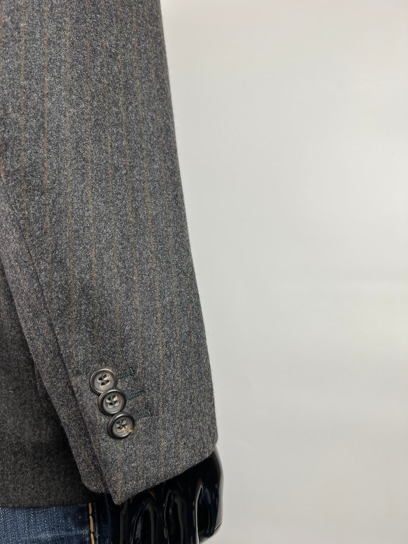 May include: A gray blazer with thin brown stripes. The blazer has a three-button cuff on the sleeve.