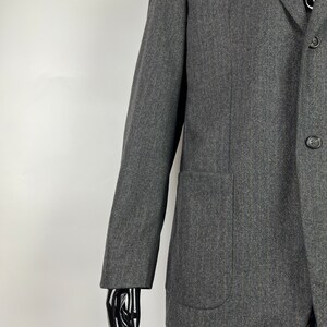May include: A dark gray blazer with a single button closure and a patch pocket on the left side. The blazer is made of a textured fabric and has a slightly relaxed fit.