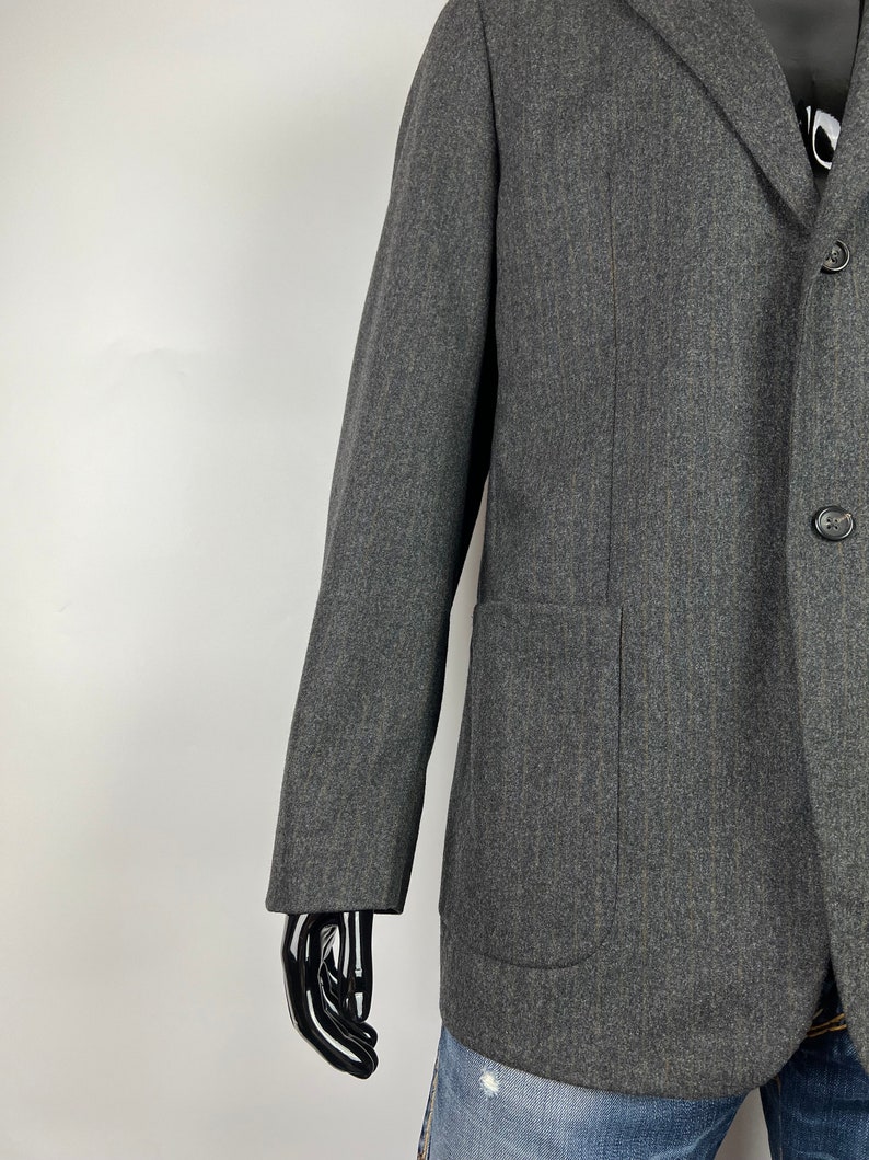 May include: A dark gray blazer with a single button closure and a patch pocket on the left side. The blazer is made of a textured fabric and has a slightly relaxed fit.