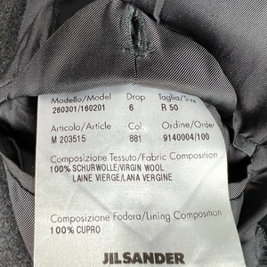 May include: A black Jil Sander clothing label with white text. The label includes the model number 260301/160201, drop size 6, size R 50, article number M 203515, color 881, order number 9140004/100, fabric composition 100% virgin wool, and lining composition 100% cupro.