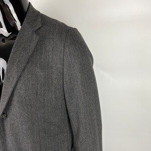 May include: A dark gray blazer with a herringbone pattern. The blazer has a two-button closure and a single pocket on the left side.