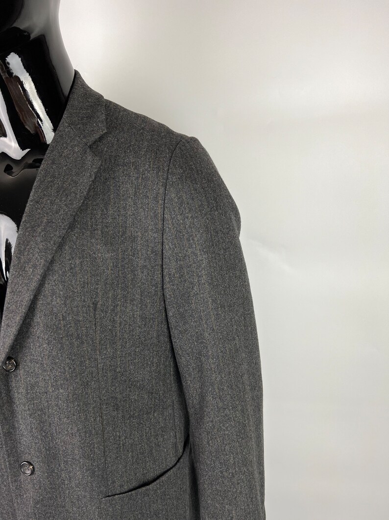 May include: A dark gray blazer with a herringbone pattern. The blazer has a two-button closure and a single pocket on the left side.