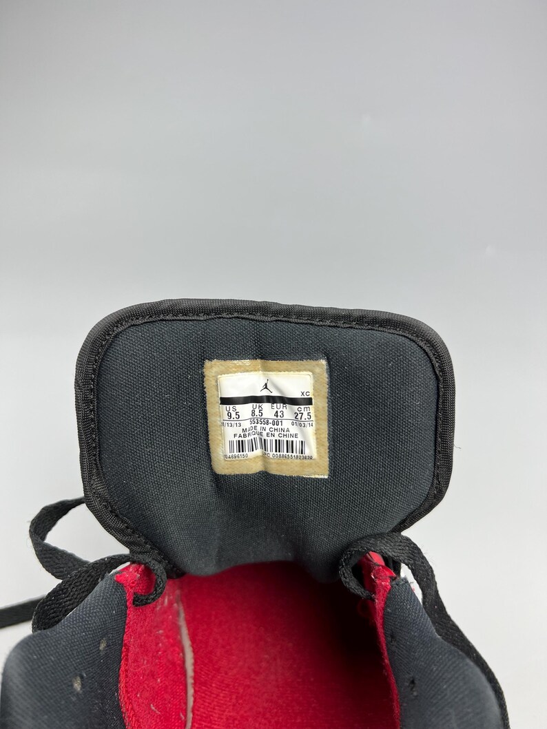 Puede incluir: Primer plano del interior de una zapatilla deportiva negra y roja. La leng&uuml;eta del zapato presenta una etiqueta con informaci&oacute;n sobre la talla y la fabricaci&oacute;n, incluyendo la talla US 9.5, la talla EUR 43 y la fecha de fabricaci&oacute;n 01/03/14.