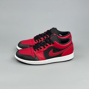 Puede incluir: Un par de zapatillas bajas rojas y negras con suela blanca. Las zapatillas presentan un logotipo swoosh rojo en el lateral y cordones negros. Adecuadas para deportes y uso diario.