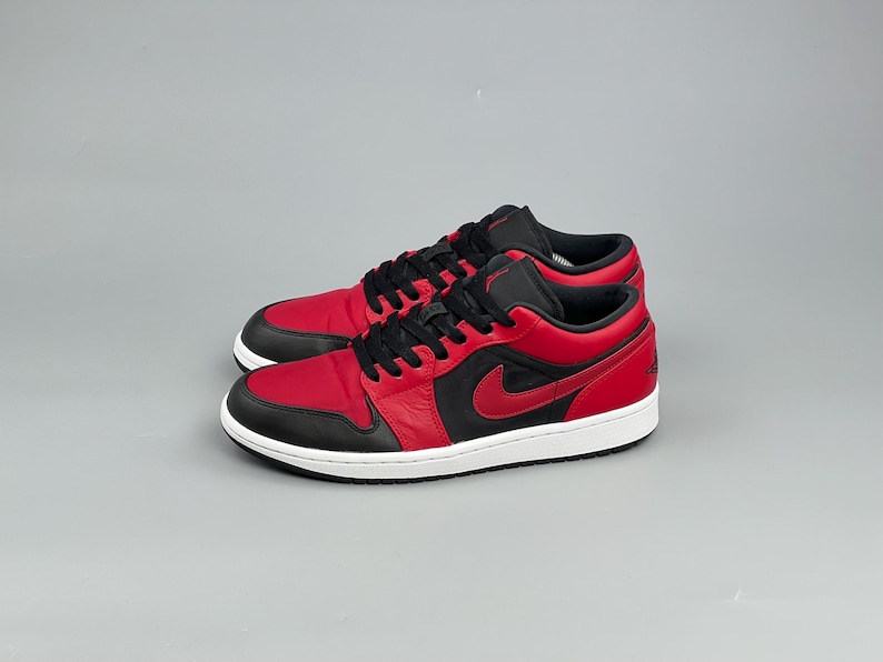 Puede incluir: Un par de zapatillas bajas rojas y negras con suela blanca. Las zapatillas presentan un logotipo swoosh rojo en el lateral y cordones negros. Adecuadas para deportes y uso diario.