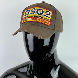 May include: A brown baseball cap with a yellow and red patch that says "DSQ2", "DSQUARED2 LOW SPEED PARACHUTE", "PART NO. 1064 LIMITED TO USE IN AIR".