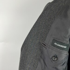 May include: A gray wool blazer with a black Jil Sander label on the inside pocket.