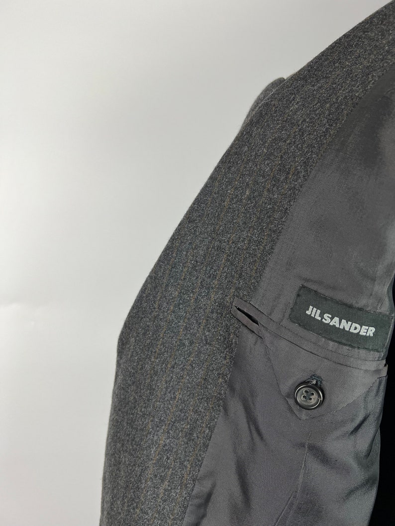 May include: A gray wool blazer with a black Jil Sander label on the inside pocket.