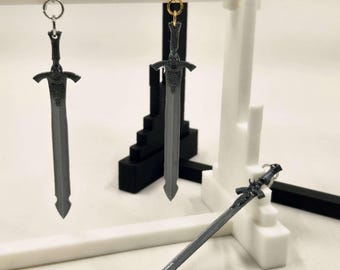 May include: Gray sword-shaped earrings with detailed hilts and blades, displayed on a white and black stand. One pair has silver hooks, the other has gold hooks. A single sword charm rests on the surface.