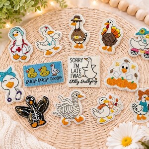 May include: A collection of embroidered patches featuring various goose designs, including a nurse, a pilgrim, a turkey, a mummy, a skeleton, and geese with pumpkins or coffee. Two rectangular patches feature the text Duck Duck Goose and Sorry I'm Late I Was Dilly Dallying.