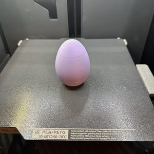 May include: A light purple 3D printed egg-shaped object on a gray textured surface. The text on the surface reads "PLA/PETG 30-50°C/50-70°C Avoid contact with solvent. Clean only with damp cloth. Adjust suggested printing temp according to material. Avoid printing ABS on Lo-Temp surface. Plate Identification Code is of Bambu PEI Plate."