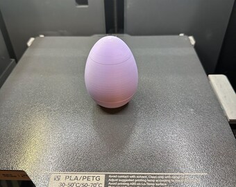 May include: A light purple 3D printed egg-shaped object on a gray textured surface. The text on the surface reads "PLA/PETG 30-50°C/50-70°C Avoid contact with solvent. Clean only with damp cloth. Adjust suggested printing temp according to material. Avoid printing ABS on Lo-Temp surface. Plate Identification Code is of Bambu PEI Plate."