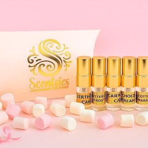 May include: A collection of perfume bottles with gold caps and labels, next to a box with the word "Scentsies" and marshmallows on a pink background. The labels read "Birthday Cake", "Butter Frost", "Carnation Cake", "Choco Cream", "Cotton Marsh", and "Pink Cake".