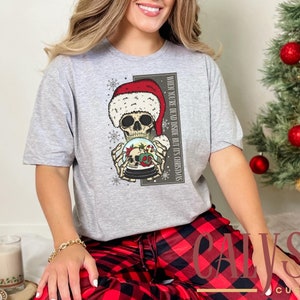 May include: Gray t-shirt with a skeleton wearing a Santa hat holding a snow globe. The text on the shirt reads "When you're dead inside but it's Christmas".