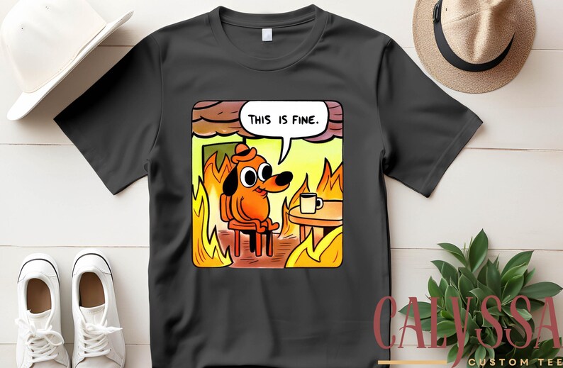 May include: Black t-shirt featuring a cartoon dog in a burning room, with the text "THIS IS FINE" in a speech bubble. The dog is orange and wearing a hat, sitting in a chair with a coffee cup on a table. The shirt is a custom tee.