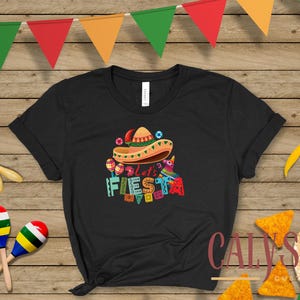 May include: Black t-shirt with a colorful "Let's Fiesta" graphic featuring a sombrero, maracas, and a pi&ntilde;ata. The shirt is decorated with festive elements, perfect for a celebration.