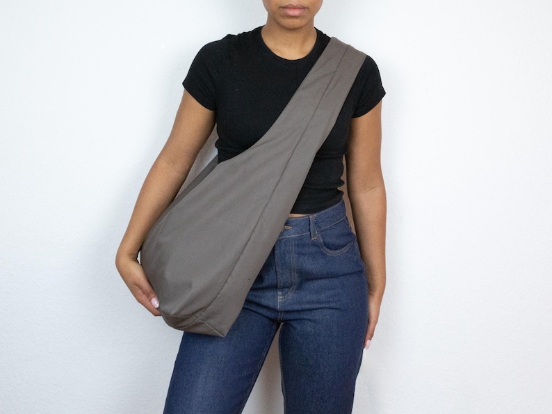 May include: A person wearing a black t-shirt and blue jeans is carrying a large, gray, fabric tote bag over their shoulder.