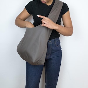 May include: A person wearing a black shirt and blue jeans is holding a large, gray, fabric tote bag.