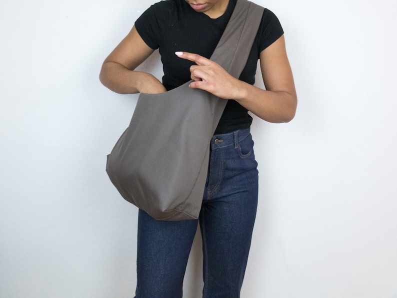 May include: A person wearing a black shirt and blue jeans is holding a large, gray, fabric tote bag.