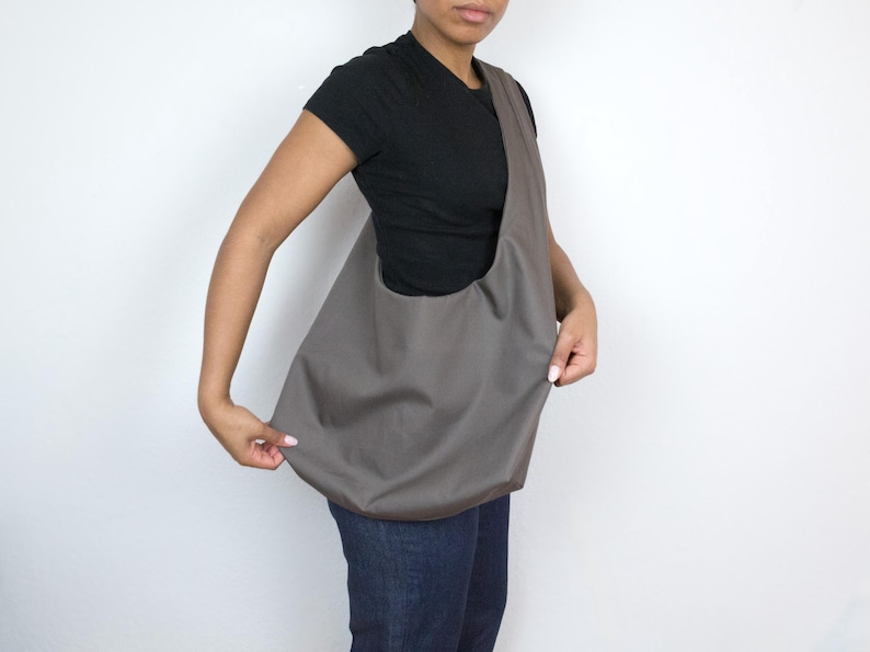 May include: A person wearing a black t-shirt and gray jeans is holding a gray canvas tote bag.
