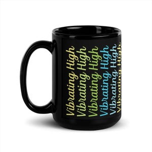 May include: Black ceramic mug with the words "Vibrating High" in a repeating pattern. The text is in a script font and gradients of yellow, green, and blue. The mug has a large handle.