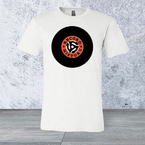 May include: White t-shirt with a black circle graphic featuring a stylised record player and the text "RECORD HISTORY" in orange.
