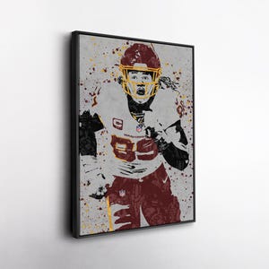 May include: Framed artwork featuring a football player in a burgundy and gold uniform. The player is wearing a helmet and jersey with the number 89. The artwork has a grunge style with paint splatter effects and the word "Washington" on the jersey.