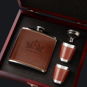 May include: A brown leather-wrapped flask with a silver lid and engraved initials "SA" and the name "Samuel Adamson". The flask is in a wooden box with two small shot glasses and a funnel.