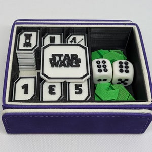以下が含まれることがあります： ゲームの駒を収納するための、黒と白のインサートが付いた紫色のベルベットボックス。インサートには、サイコロ、トークン、カード用のコンパートメントがあります。ボックスには「STAR WARS」の文字が印刷されています。
