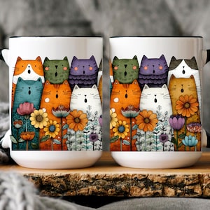 May include: Two white ceramic mugs with black handles and rims. Each mug features a colorful illustration of singing cats and flowers. The cats are in various colors, including orange, blue, and purple. The mugs are on a wooden surface.